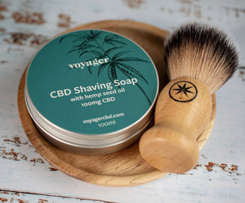 CBD Shaving Soap by Voyager with a wooden brush on a rustic surface